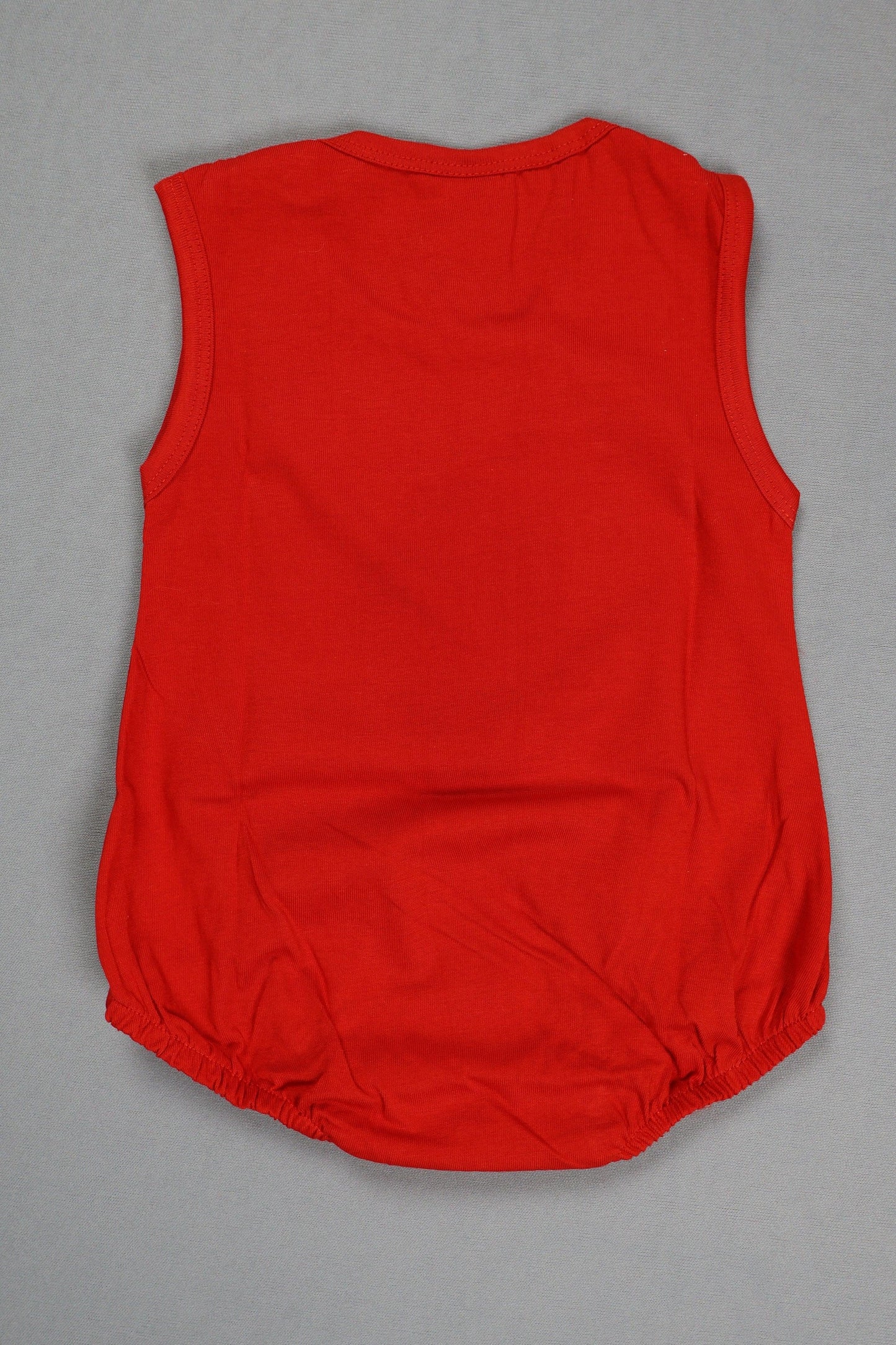 Back view of a sleeveless red cotton baby romper with elastic leg openings on grey background