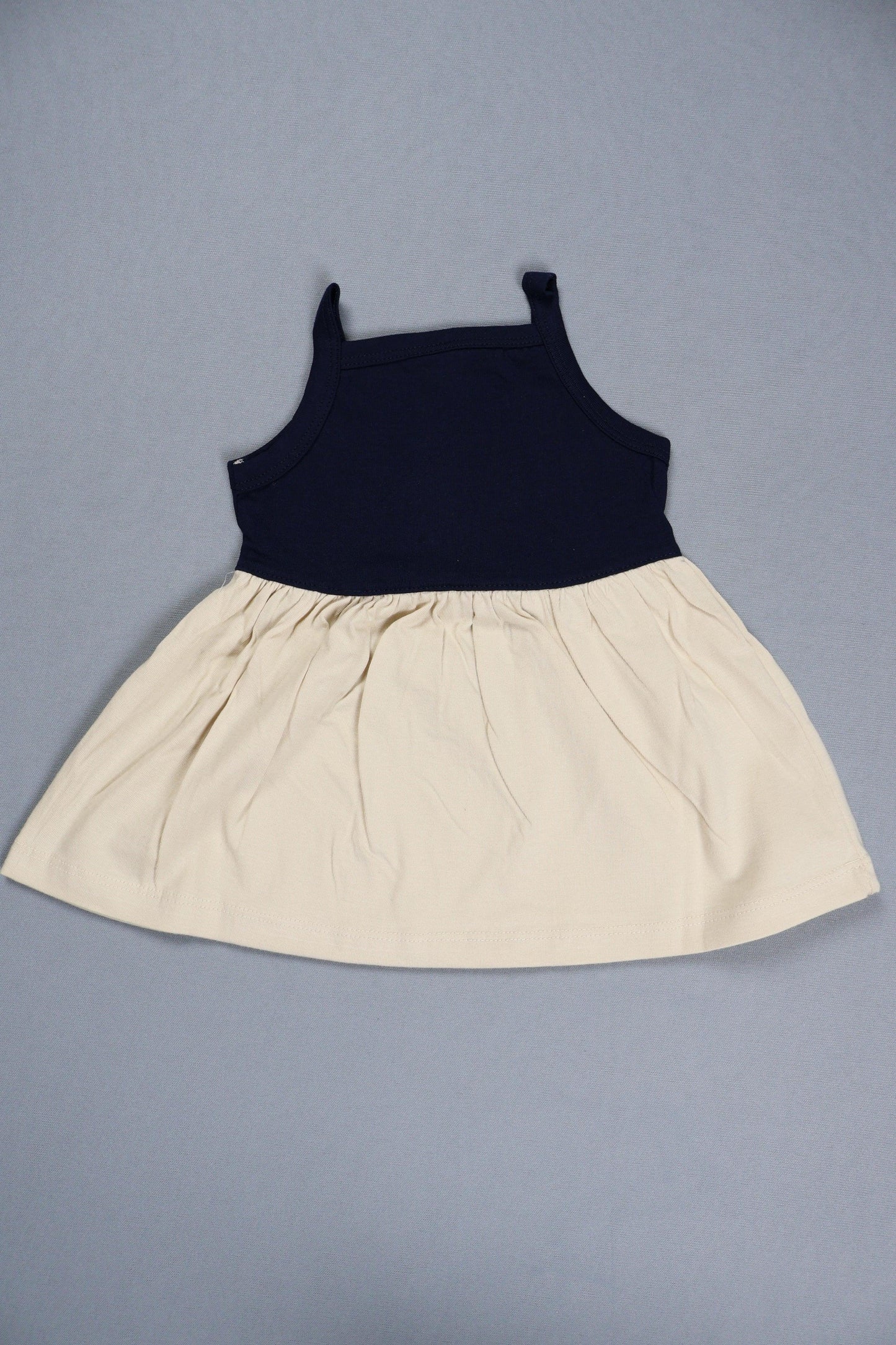 Navy and cream cotton knit strappy frock for infants, laid on a plain background