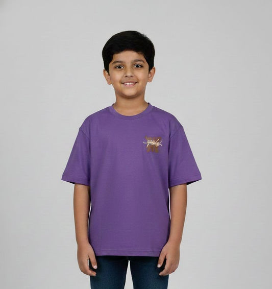 A young boy modeling a purple oversized t-shirt. The front features a small neutral-toned graphic on the chest, while the back displays a large, intricate streetwear-style typography design. He is posing against a plain grey background.