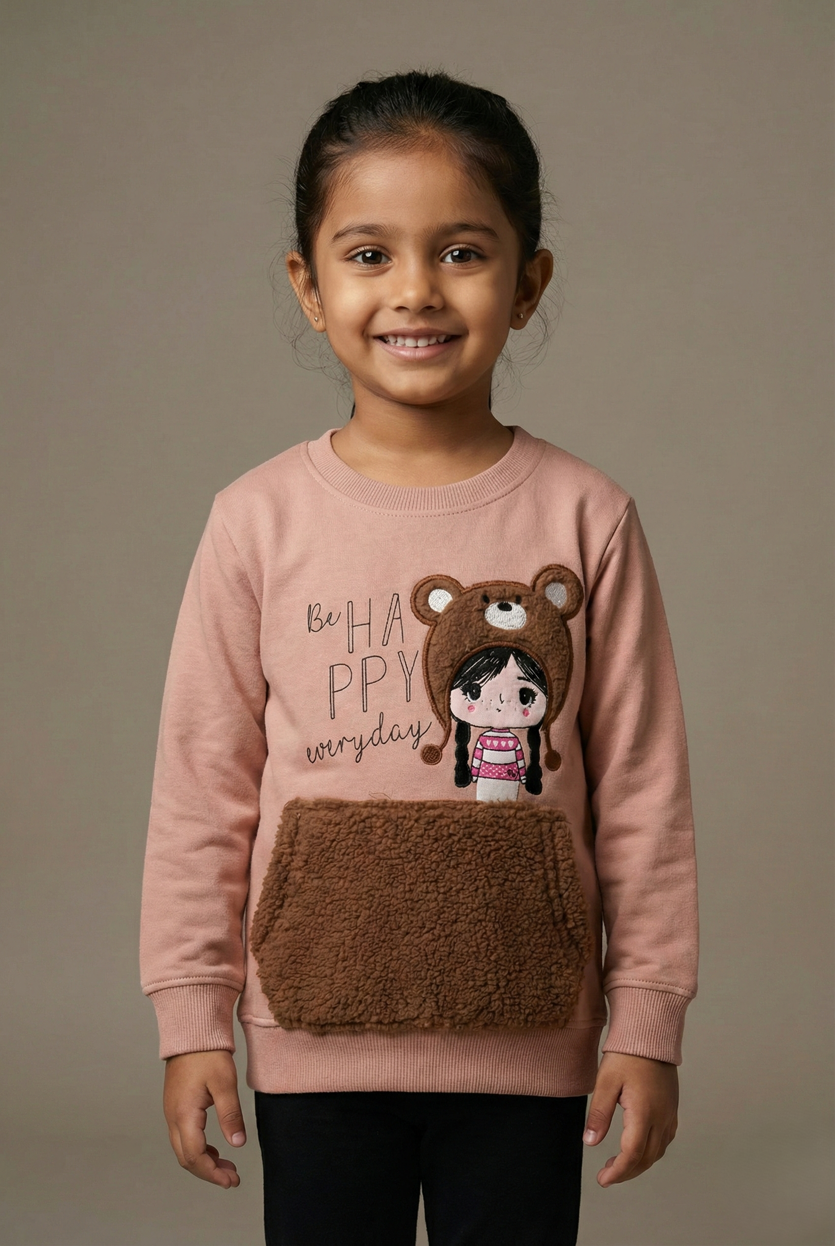 Pink long-sleeve kids sweatshirt featuring a cartoon girl wearing a bear hat, the text ‘Be happy everyday,’ and a soft brown teddy-fleece front pocket, displayed on a white background