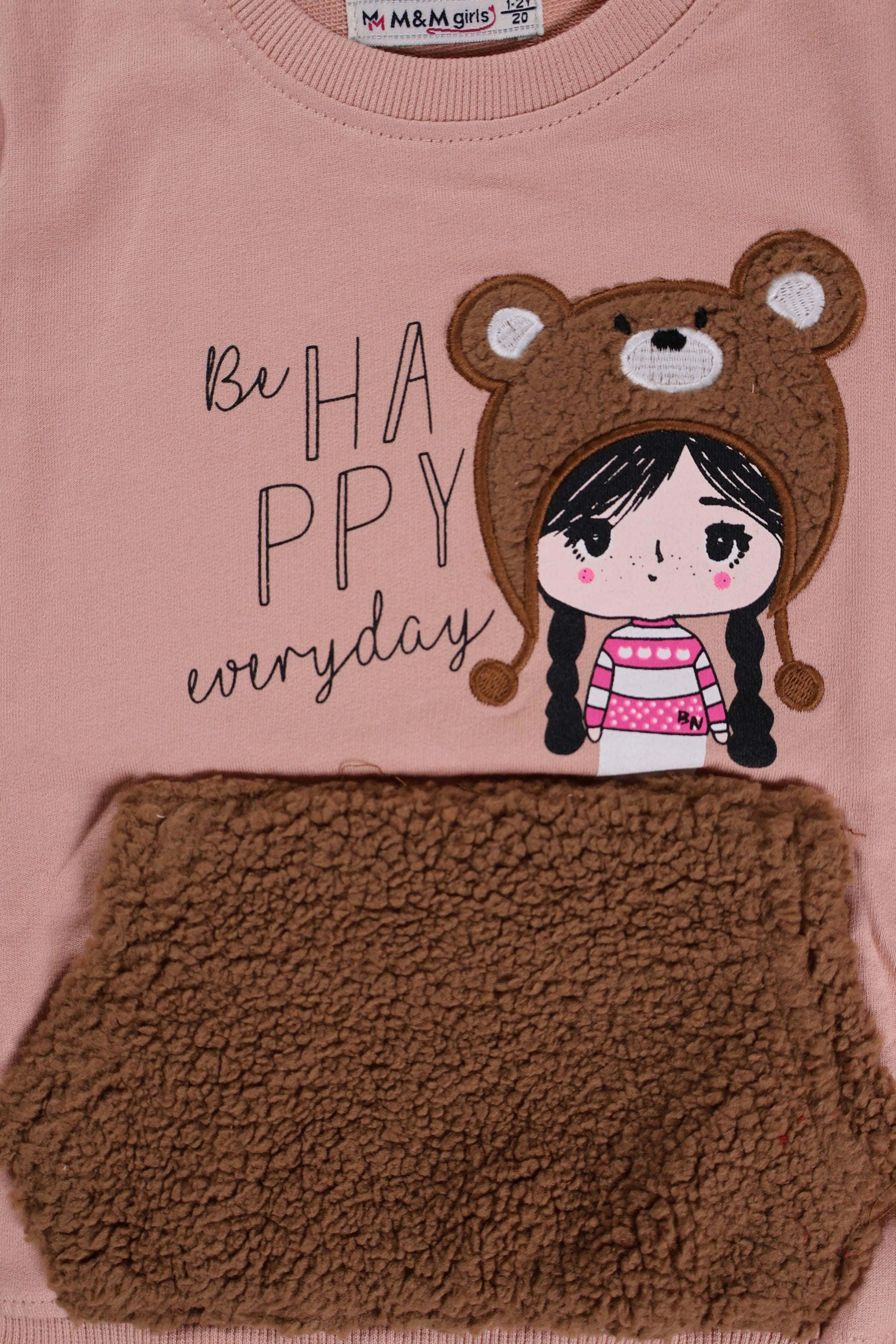 Children's pink shirt with bear-themed design and text 'Be Happy everyday' on a brown background.