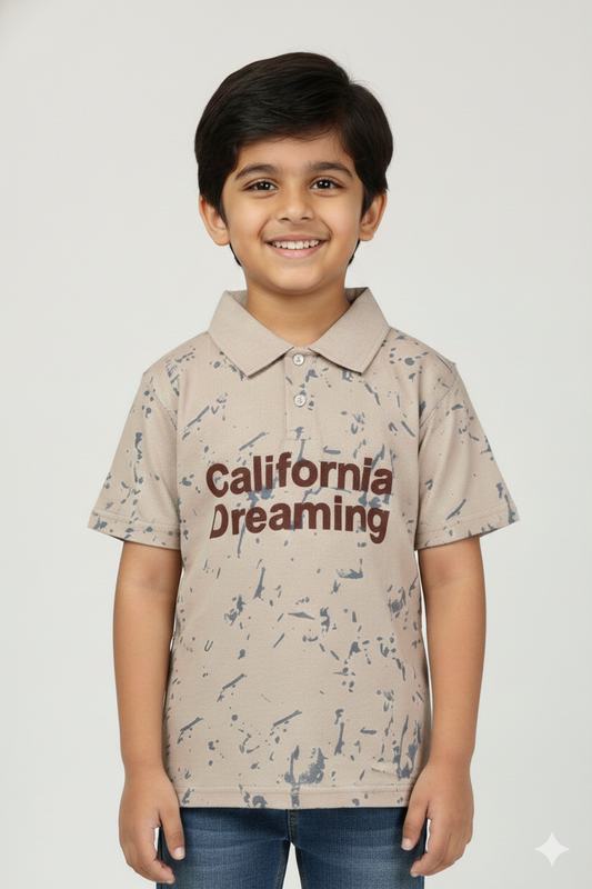 A young boy wearing a sand-colored polo t-shirt with a blue marble splatter effect. The shirt features a classic collar and the words "California Dreaming" printed in brown across the chest. He is smiling and posing against a light neutral background.