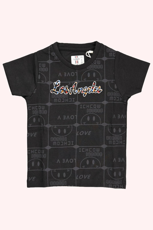 A children's black short-sleeve t-shirt. The front features "Los Angeles" written in a colorful script font over a subtle, all-over dark grey repeating "Love" typography pattern. The shirt is displayed as a flat lay against a light pink and white background.