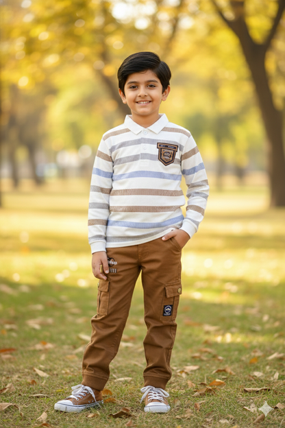 A young boy modeling a stylish two-piece autumn set. He is wearing a long-sleeve polo shirt with blue, tan, and white horizontal stripes and a small chest pocket. This is paired with tan brown cargo joggers featuring large side pockets. He is posing outdoors in a park with golden autumn leaves on the ground.