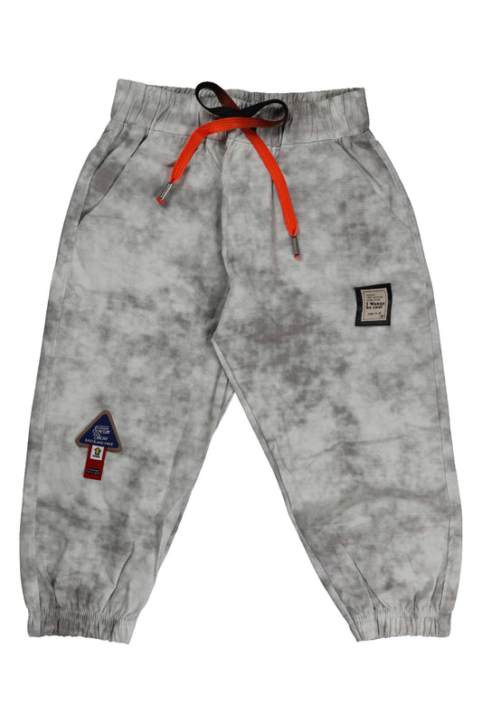 A pair of children's joggers featuring a grey marbled acid-wash pattern. The pants include a comfortable elastic waistband with a bright orange functional drawstring, ribbed ankle cuffs, and small decorative patches on the legs.