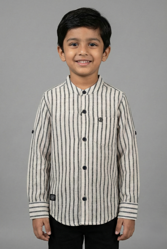 A young boy wearing a Cream and Black vertical striped full-sleeve shirt from Fyst Fashion. The shirt features a modern mandarin collar, a front chest pocket, and dark contrast buttons. The sleeves are designed with roll-up tabs for a versatile look. The image shows a front view of the child smiling against a neutral grey background.