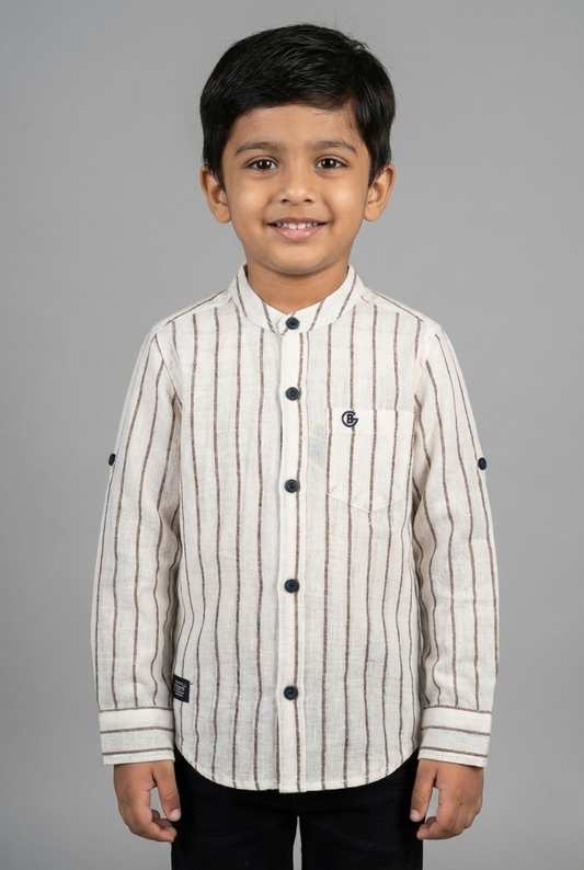 A young boy wearing a beige and brown vertical striped full-sleeve shirt from Fyst Fashion. The shirt features a modern mandarin collar, a front chest pocket, and dark contrast buttons. The sleeves are designed with roll-up tabs for a versatile look. The image shows a front view of the child smiling against a neutral grey background.