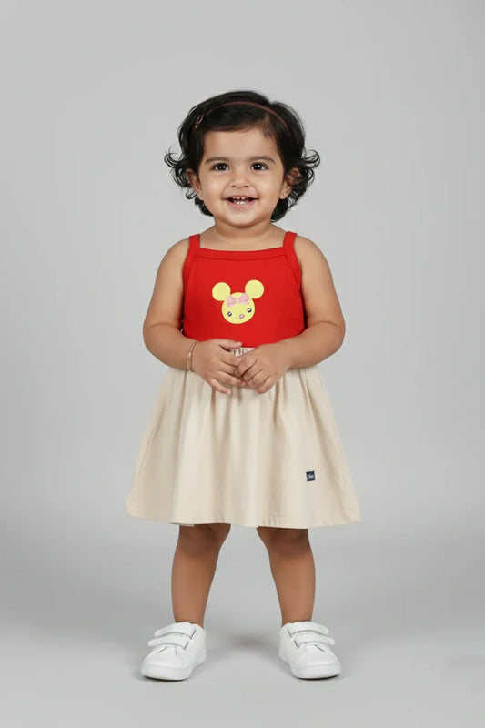 infant in red and cream sleeveless cotton frock with cartoon print, white shoes, studio background