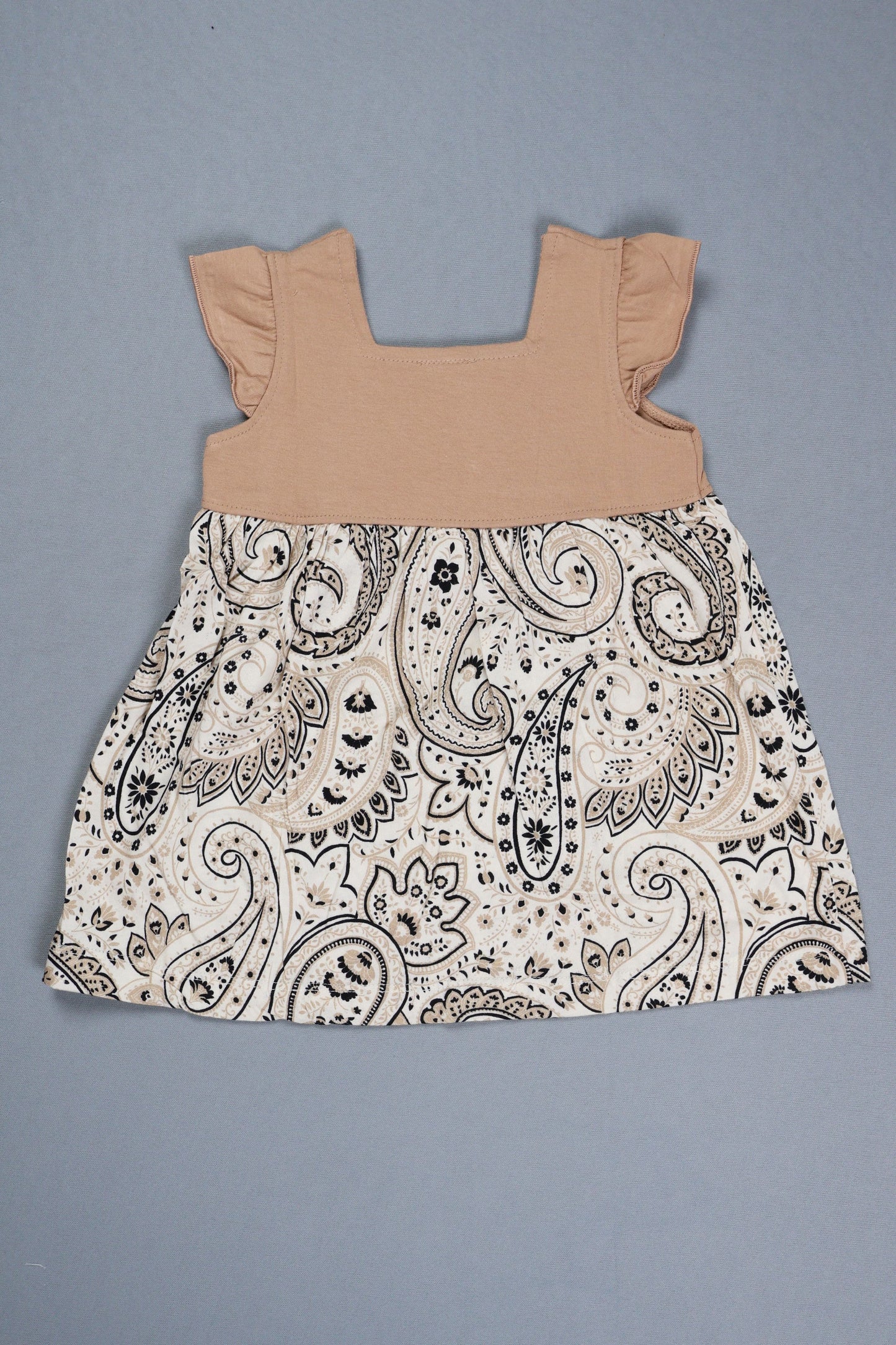 Paisley-patterned fabric and beige baby romper on a gray background