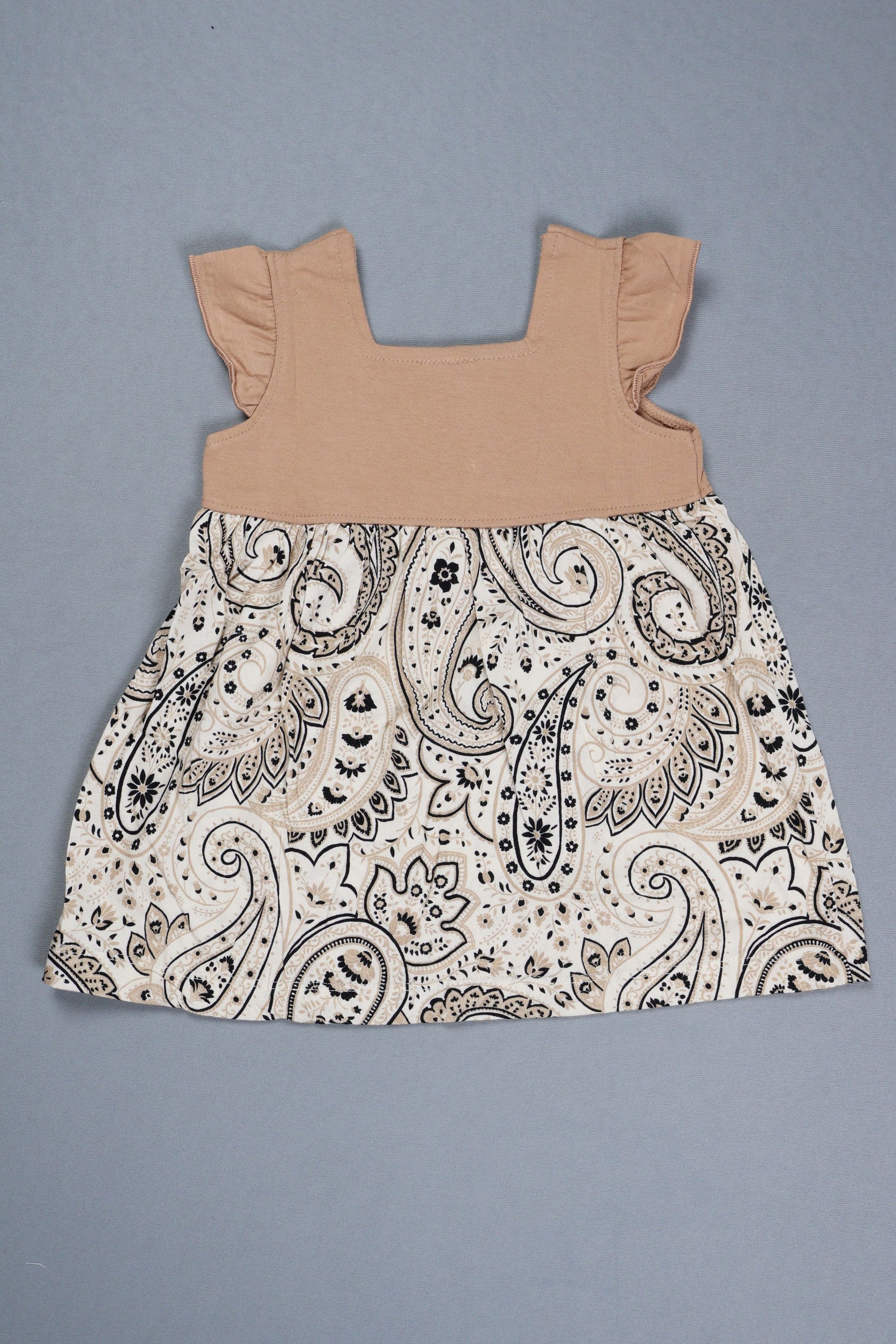 Paisley-patterned fabric and beige baby romper on a gray background